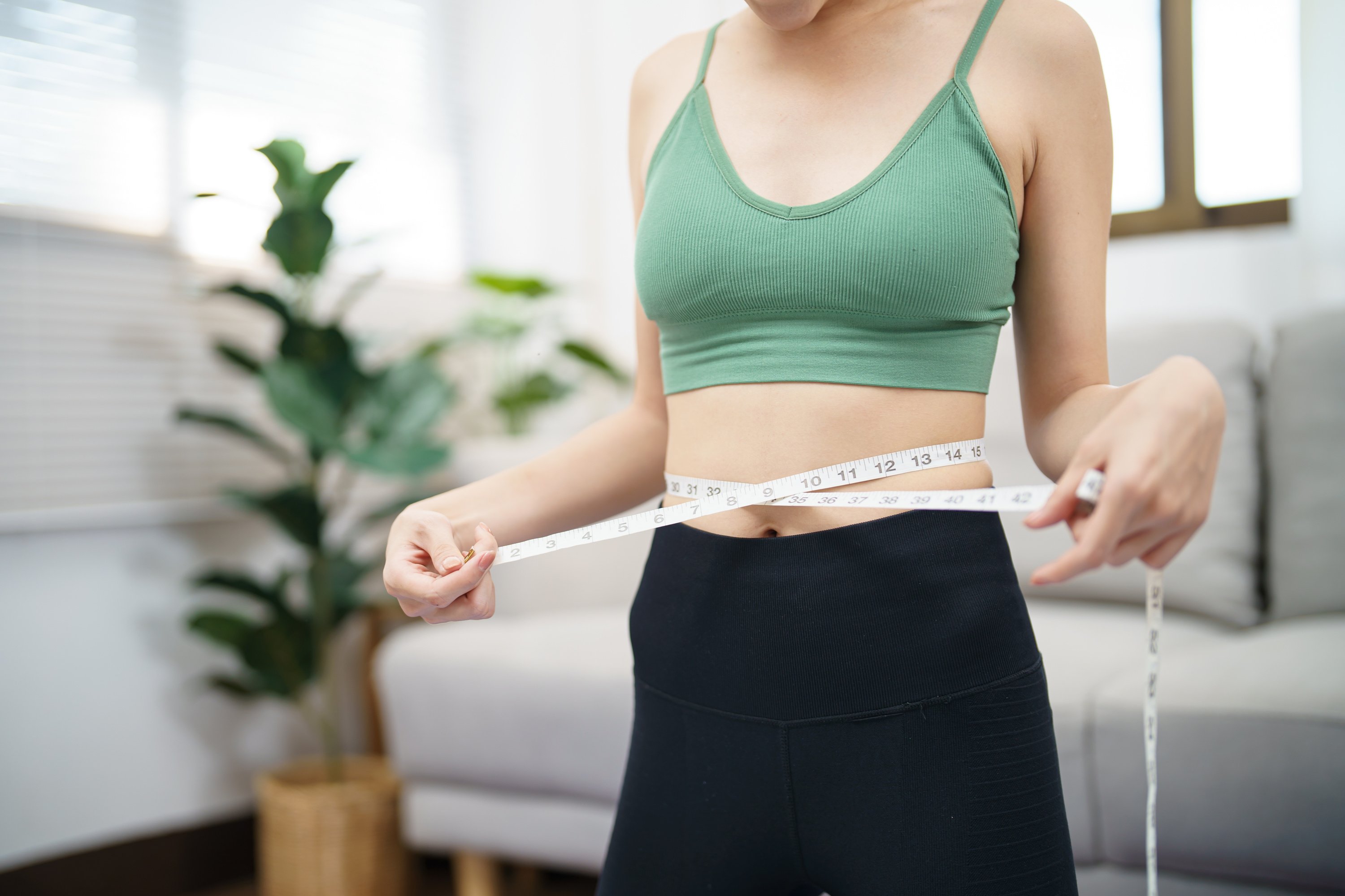 Asian healthy woman dieting Weight loss. Slim woman measuring waist with measure tape after diet at home weight control.